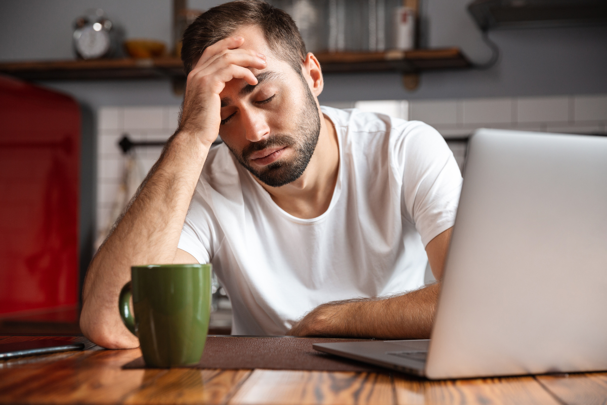 A man tired at his desk with his head in his hand, wondering how his hormones impact his tiredness